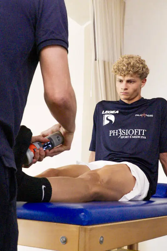 Fisioterapista che utilizza un dispositivo elettromedicale avanzato per il trattamento della caviglia di un giovane atleta.